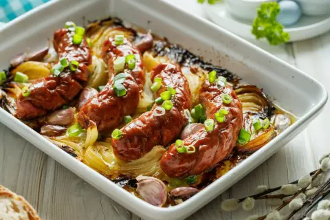 Pyszna, pieczona biała kiełbasa z cebulą i czosnkiem, posypana szczypiorkiem. Idealna na wielkanocny stół.