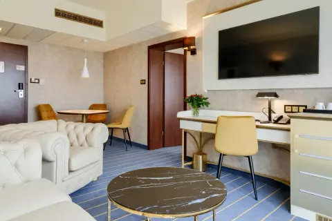 Elegancki pokój w hotelu Diament Wrocław: wygodna sofa, biurko z telefonem i TV, stolik kawowy i okrągły stół z krzesłami.