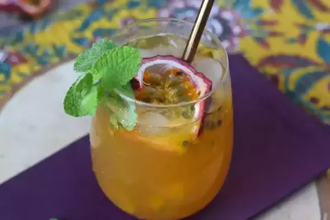 Un délicieux cocktail thé glacé aux fruits de la passion, garni de menthe fraîche et d'une tranche de fruit.