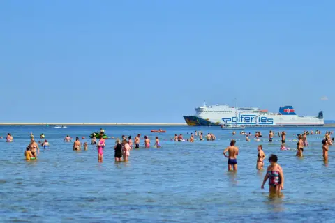Ludzie kąpią się w morzu, a w tle płynie prom Polferries, który kursuje na trasie Świnoujście - Ystad.