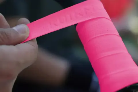 Mano applica nastro rosa su manubrio bici, mostrando la differenza tra grip e overgrip.