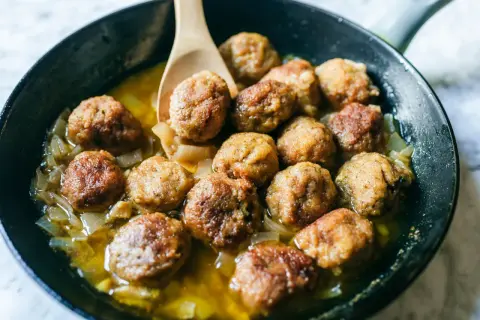 Polpette in bianco dorate e succulente, cotte in padella con cipolle dolci e un sughetto invitante. Un classico confortante.