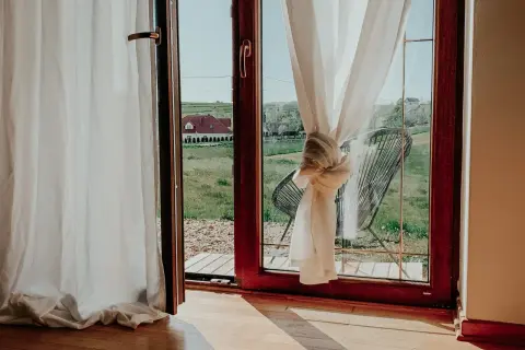 Jak upiąć za długie firanki? Węzeł na zasłonie przy oknie z widokiem na wieś.