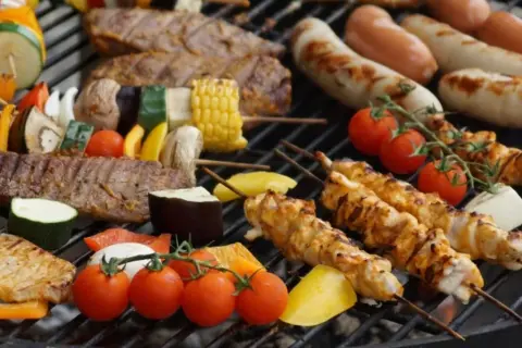 Na ruszcie grilluje się zdrowy grill: szaszłyki z kurczaka, wołowiny i warzyw, kiełbaski, pomidorki i kukurydza.