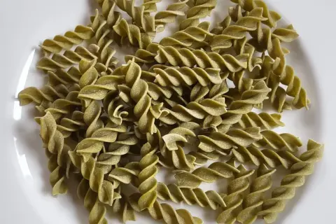 Zielone fusilli, czyli makaron z zielonego groszku, ułożone na białym talerzu.