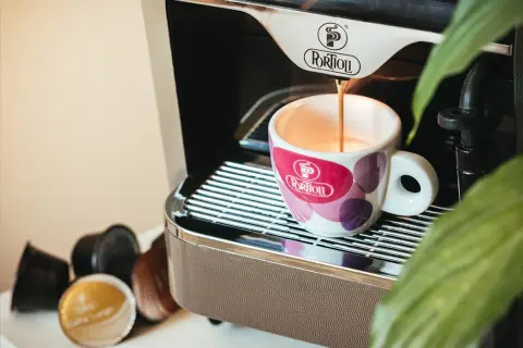 Espresso pouring into a patterned cup next to coffee capsules and a coffee machine.