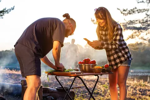 Ein Paar bereitet draußen Gemüse zu, während die Sonne untergeht. Sie kochen im Wohnmobil und genießen die Natur.