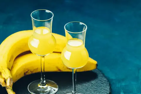 Dwa kieliszki z żółtym płynem, obok kiść bananów. To idealny moment na domową nalewkę z banana.