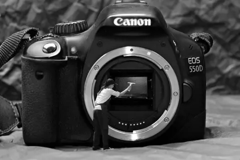 Miniaturowa postać czyści wnętrze aparatu Canon EOS 550D, pokazując, jak wyczyścić matrycę w aparacie.