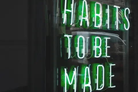 Zielone neony "HABITS TO BE MADE" przypominają o psychologii systemu nagród i kar, który kształtuje nasze nawyki.