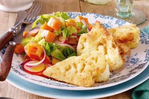 Knuspriges Blumenkohl Schnitzel mit einem bunten Salat aus Kürbis, Radieschen und roten Zwiebeln auf einem blumengemusterten Teller.