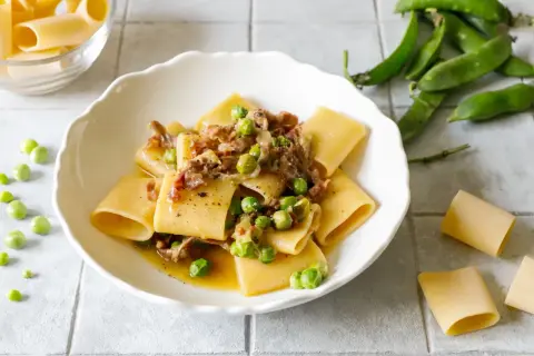 Piatto di paccheri conditi con piselli freschi e pezzetti croccanti di prosciutto crudo, un classico saporito.