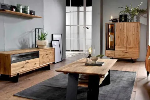 Przytulny salon w stylu boho loft. Drewniane meble, szara ściana i duża przeszklona drzwi tworzą ciepłą atmosferę.