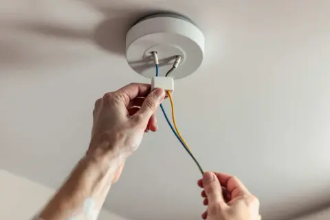 Mains électriques connectées pour installer un plafonnier. Les fils colorés sont manipulés avec soin.