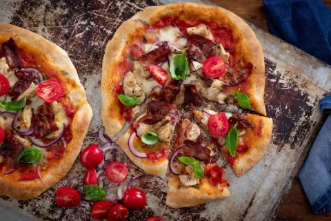 Två läckra pizzor med kyckling och bacon, toppade med körsbärstomater och basilika.