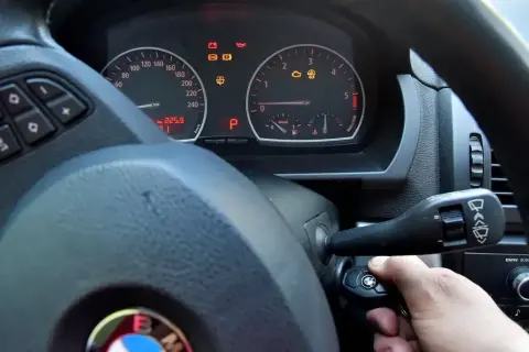 Ręka przekręca kluczyk w stacyjce BMW. Kontrolki na desce rozdzielczej świecą, ale rozrusznik nie kręci tylko cyka.