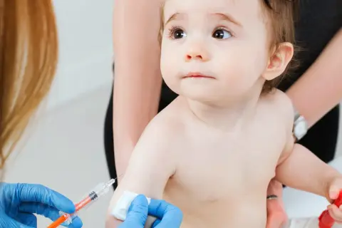 Małe dziecko otrzymuje szczepienie RSV. Ręka w niebieskiej rękawiczce trzyma strzykawkę, przygotowując się do podania zastrzyku.