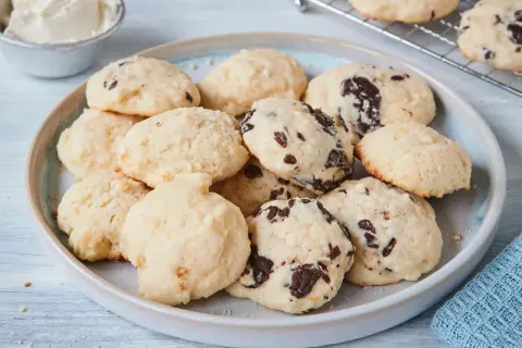 Leckere Cheesecake Cookies mit Schokoladenstückchen auf einem Teller, daneben eine Schüssel Frischkäse.