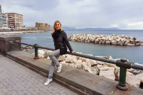 Donna sorridente sul lungomare di Napoli, con Castel dell'Ovo e il mare sullo sfondo. Un'ottima idea per cosa vedere a Napoli centro.