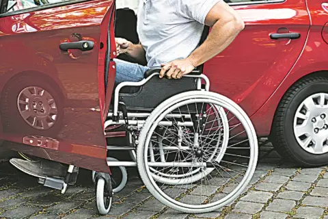 Un uomo in carrozzina si prepara a salire in un'auto rossa. Un caregiver ha aiutato nell'acquisto di un'auto adatta.