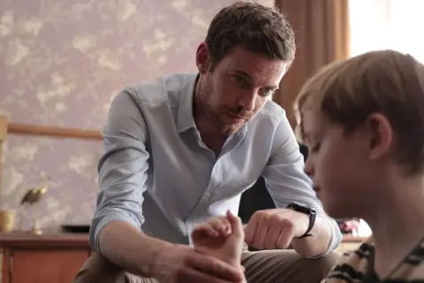 Ein Mann spricht mit einem Jungen, dessen Hand er hält. Die Szene erinnert an die Serie "Chemie des Todes".