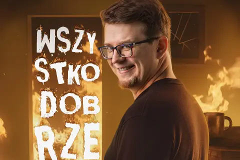 Mieszko stand up w płomieniach, z napisem "WSZYSTKO DOBRZE". Uśmiechnięty mężczyzna w okularach na tle ognia.