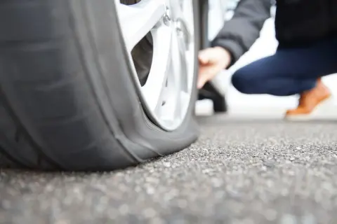 Une personne accroupie examine un pneu crevé, signe qu'il faut s'arrêter et changer la roue.