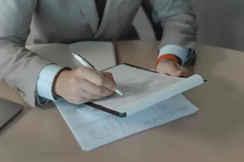Rekruter w garniturze podpisuje dokumenty. Praca rekrutera to często analiza CV i rozmowy.