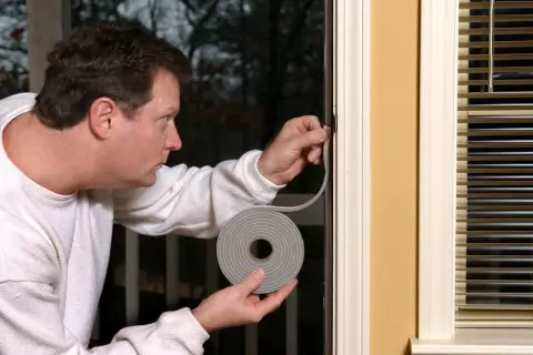 Mann dichtet undichte Fenster mit Dichtungsband ab, um Zugluft zu vermeiden.