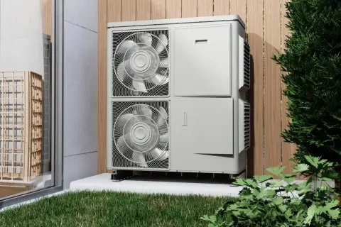 Unidad exterior de bomba de calor, eficiente en su caldera eléctrica consumo, instalada junto a una valla de madera y vegetación.