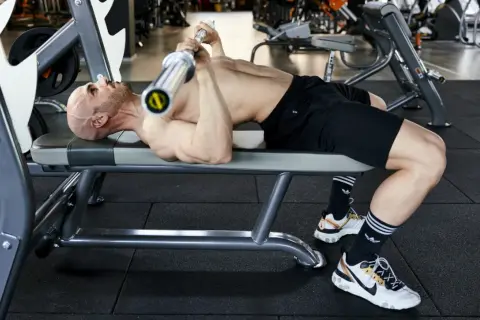 Uomo calvo si allena in palestra, sollevando un bilanciere su una panca. Un esempio di **super serie palestra** per un allenamento intenso.