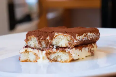 Ein Stück original italienisches Tiramisu, üppig mit Kakao bestäubt, auf einem weißen Teller.
