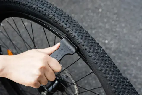 Dłoń używa czarnej łyżki do opon rowerowych, aby zdjąć oponę z obręczy. To pokazuje, jakie łyżki do opon rowerowych są potrzebne do naprawy.