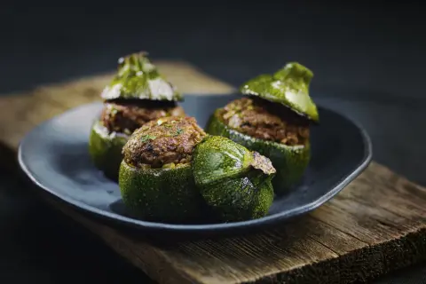 Trois courgettes rondes farcies, garnies d'une préparation savoureuse, reposent sur une assiette sombre, posée sur un plateau en bois vieilli.