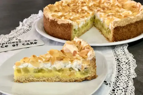 Ein köstlicher Rhabarberkuchen mit Pudding und Baiser, bestreut mit Mandelblättchen. Ein Stück Glück auf einem Teller.