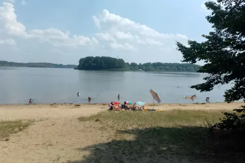 Słoneczny dzień nad jeziorem Przeczyckim. Ludzie kąpią się i odpoczywają na piaszczystej plaży.