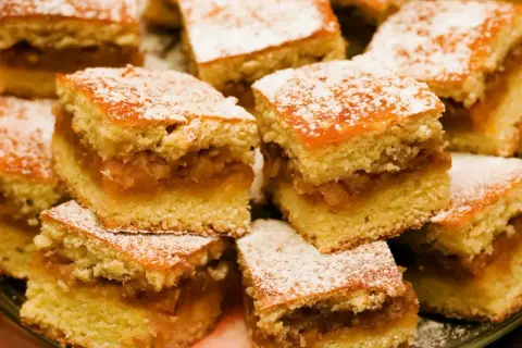 Szybkie ciasto z jabłkami, pokrojone w kostkę i posypane cukrem pudrem, wygląda apetycznie. Idealne na deser.