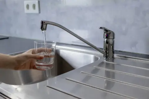 Un vaso se llena de agua bajo un grifo moderno, mostrando la buena presión del agua del grifo.