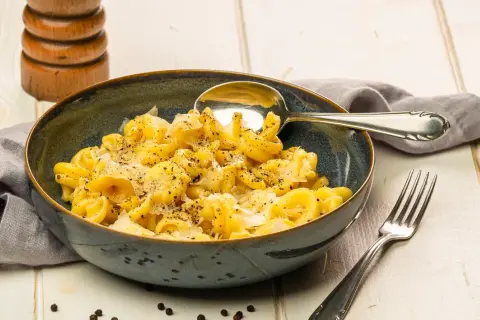 Eine Schüssel Pasta mit cremiger cacio e pepe sauce, bestreut mit frisch gemahlenem Pfeffer. Daneben liegen ein Löffel und eine Gabel.