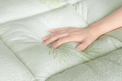 A hand rests on a quilted, light green mattress with a subtle bamboo leaf pattern. Experience the comfort and breathability of bamboo sleeping mat benefits.