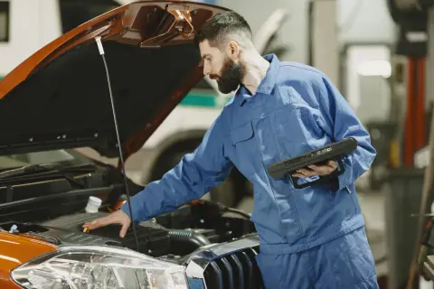 Mechanik sprawdza silnik, szukając rozwiązania, jak zamocować luźną osłonę pod silnikiem do zderzaka.