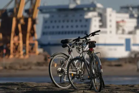 Dwa rowery czekają na swój rajd rowerowy przy nabrzeżu. W tle ogromny statek wycieczkowy i dźwigi portowe.