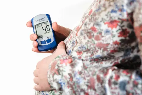 Gravid kvinna kontrollerar sitt blodsocker med en glukosmätare. En viktig del av att hantera graviditetsdiabetes.