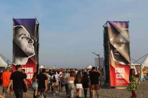 Ingresso per il festival con gigantografie di Carl Cox e Joseph Capriati. La folla si muove sulla sabbia.