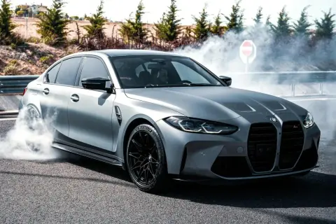 Srebrne BMW M3 G80 w poślizgu, z opon dymiących na asfalcie.