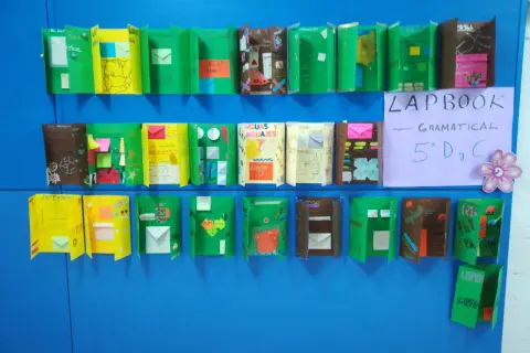 Varias ideas de lapbook creativos, con solapas y sobres, exhibidos en una pared azul.