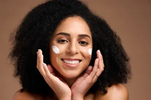 Une femme souriante avec des touches de crème sur les joues, profitant des bienfaits du beurre de karité visage pour une peau douce et hydratée.