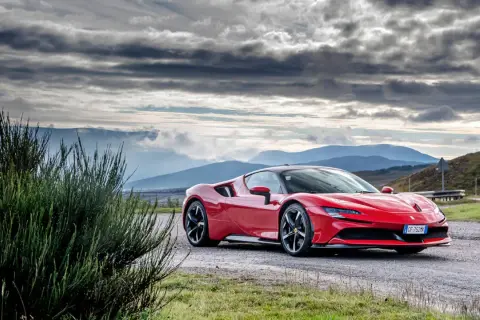 Czerwone Ferrari SF90 na tle gór i burzowego nieba.