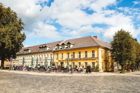 Gemütliche Straßencafés beleben die sonnige Rheinsberg Altstadt. Menschen sitzen unter grünen Sonnenschirmen vor gelben Fachwerkhäusern.