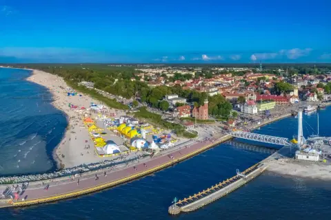 Ustecka plaża tętni życiem, pełna kolorowych namiotów i ludzi. W tle widać urokliwe miasteczko i port. To idealne ustka atrakcje dla każdego.